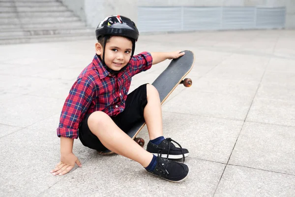 小男孩坐在沥青附近他的滑板 — 图库照片