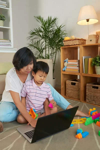 亚洲母亲和儿子坐在地板上 看着电脑上的东西 — 图库照片