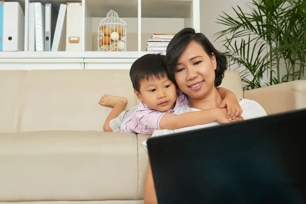 Liten Pojke Kramar Hans Mor Bakifrån När Hon Arbetar Laptop — Stockfoto