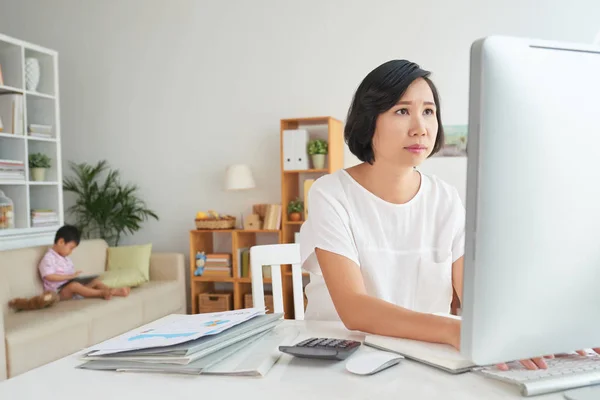 Asian woman busy with work on computer when her son is playing
