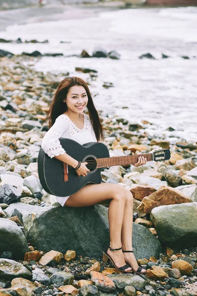 美丽的越南女孩坐在岩石上的海边和弹吉他 — 图库照片