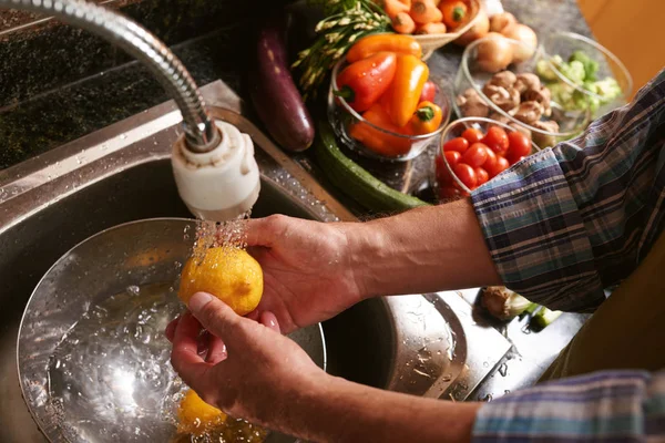 Hands of man washing lemons and vegetables in kitchen sink