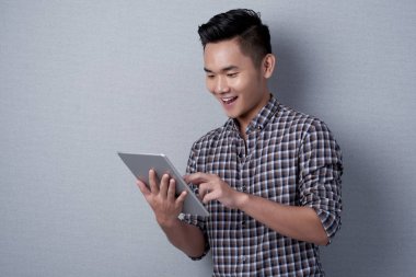 Cheerful Vietnamese man surfing net on modern digital tablet clipart