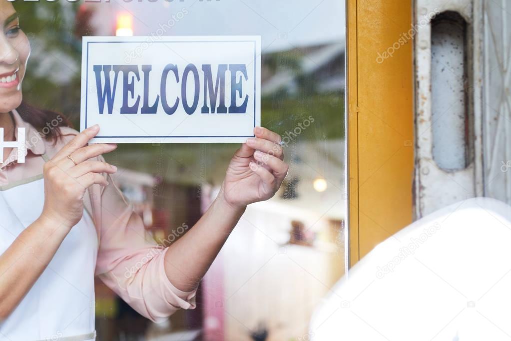 Cheerful young Vietnamese shop owner turning welcome sign on the glass door