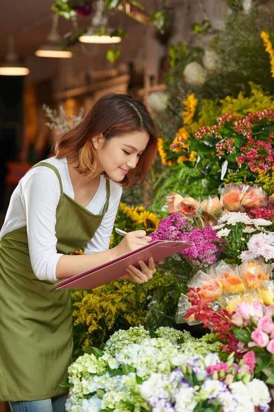 魅力的なアジアの花ショップ在庫 肖像画店をしながら必要な情報を書き留めて所有者着てエプロン — ストック写真