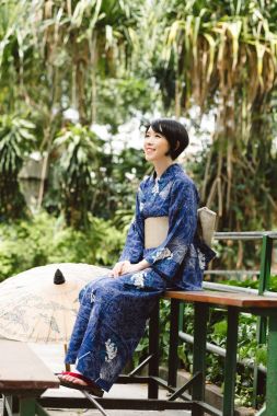 Bahçede bankta oturmuş geleneksel kimono içinde gülümseyen güzel Japon kadın