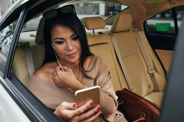 車に座っているとき 彼女のスマート フォンで音楽を聴くイヤホンで魅力的な女性 — ストック写真