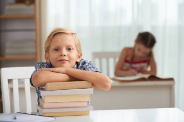 Kitap yığını eğilerek ve kameraya bakarak akıllı çocuk gülümseyen