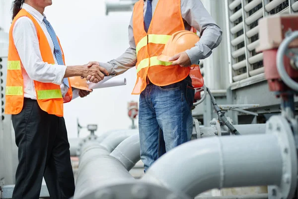 Plant engineer with blueprints and worker shaking hands