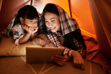 Anne ve kızı dijital tablet gösterir izlerken battaniyenin altında