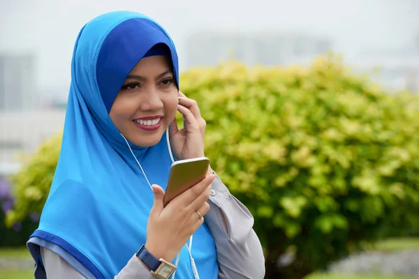 戴头巾的年轻漂亮女人的肖像手持智能手机 听音乐和微笑 — 图库照片
