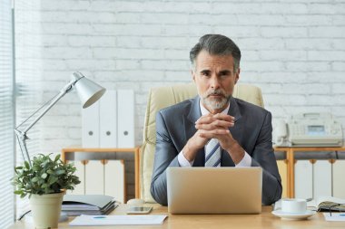 Onun masada oturan ve kameraya bakarak olgun işadamı portresi