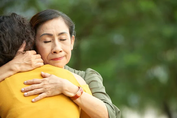 目を閉じて彼女の巻き毛の娘を優しく抱きしめるはかなり年配の女性の肖像画のショット — ストック写真