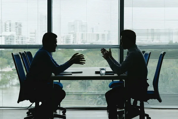 Silhouettes of business people sitting at table against the office window and discussing various issues