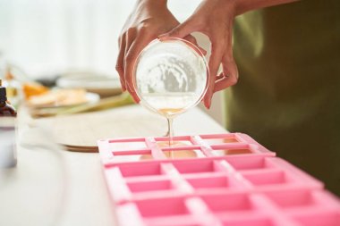 Close-up image of woman pouring soap mixture into plastic form clipart
