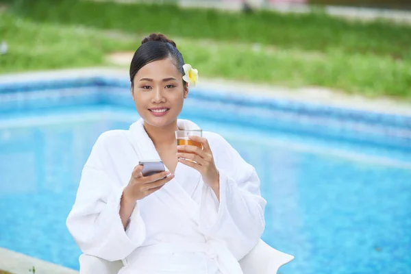 美丽的越南青年妇女放松池与玻璃的新鲜果汁和智能手机 — 图库照片