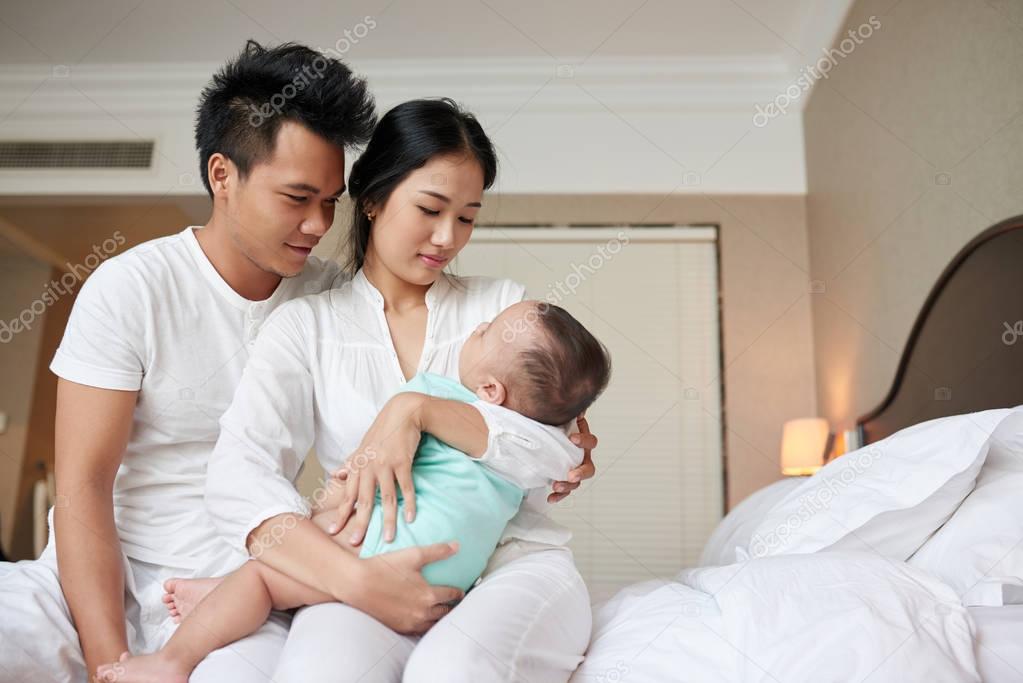 Young Vietnamese family with infant boy sitting in bedroom