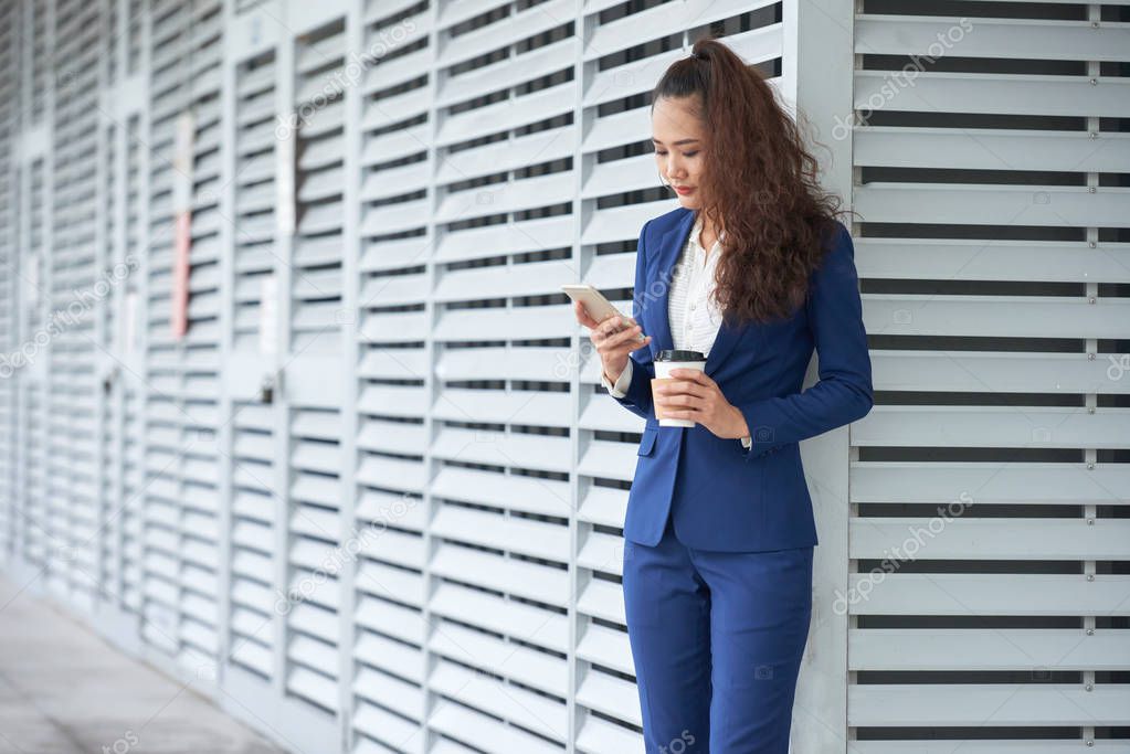 Business lady drinking coffee and checking messages in her smartphone