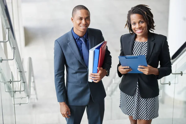 Happy young African-American business people with documents looking at camera