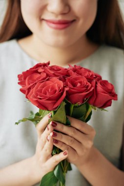 Gülümseyen genç kadının elinde kırmızı gül buketi