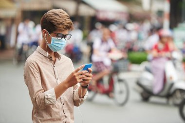 Uyarı iletisi smartphone cep telefonu ile kontrol yüzü maskeli Asya genç adam