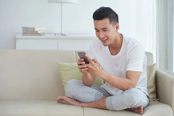 Joven Hombre Vietnamita Emocionado Sentado Casa Utilizando Aplicación Teléfono Inteligente —  Fotos de Stock