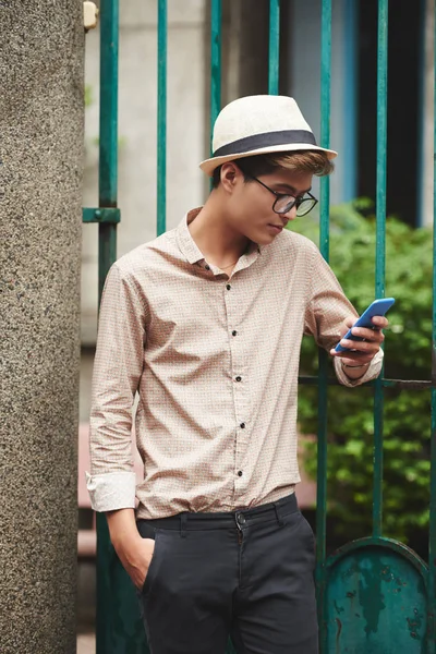 魅力的なアジアの若者屋外で立って 彼のスマート フォンでニュースを読む — ストック写真