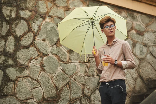 年轻的亚洲男人带着黄色的雨伞走着听音乐 — 图库照片