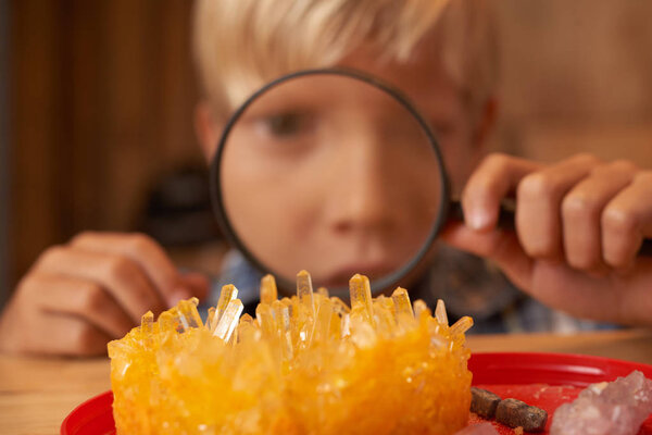 Boy looking on crystals he grown through magnifying glass