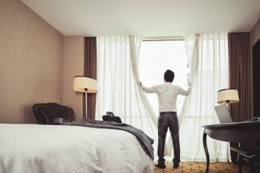 Otel odasında perdeleri açmayı işadamı arkadan görünüş
