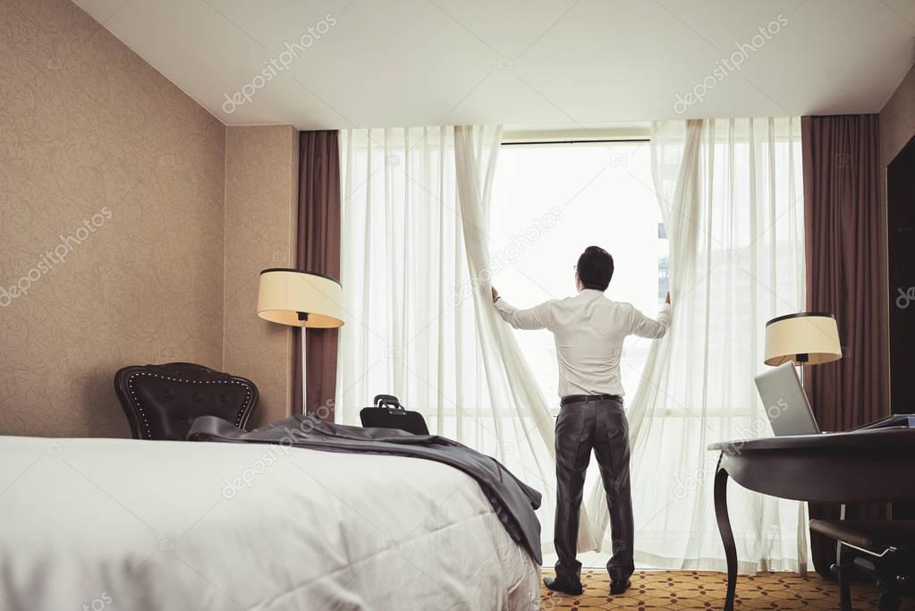 Rear view of businessman opening curtains in hotel room