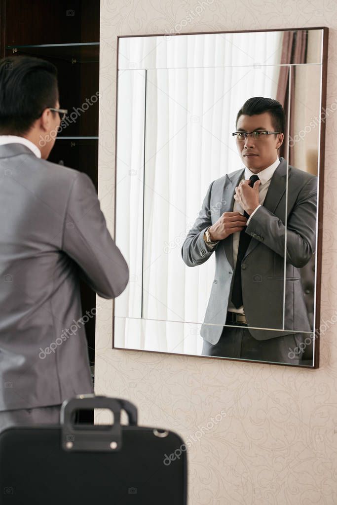 Serious Vietnamese businessman adjusting tie in front of mirror