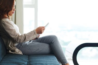 Genç Asyalı kadın kanepede oturan ve okuma şey dijital tablet yan görünüm