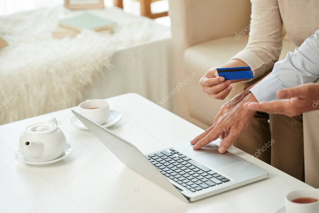 Hands of old couple paying bills online with credit card