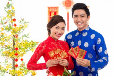 Geleneksel kostümler giymiş ve elinde, ay yeni yıl sunulan renkli zarf tutan Vietnamca çift gülümseyen