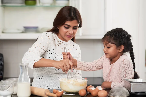 Cute Indian girl helping her beautiful middle-aged mother to beat eggs