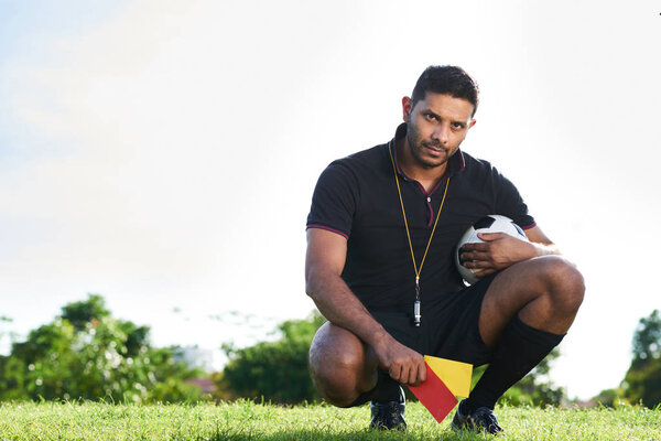 mixed race soccer referee sitting on haunches with ball and penalty cards 