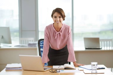 Onu masaya yaslanmış çekici gülümseyen kadın girişimci portresi