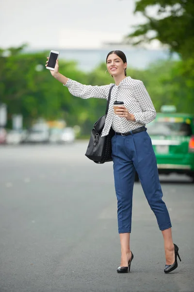 通りでタクシーをキャッチしようとテイクアウトのコーヒーを飲みながら美しい若い女性 — ストック写真