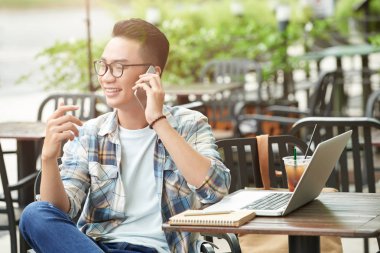 Açık kafede oturan ve telefonda konuşurken neşeli serbest meslek