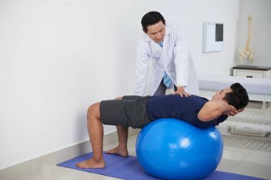 Genç Vietnamlı terapist kontrolü altında fitness Ball egzersizleri yapıyor