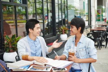 Neşeli Asya genç insanlar içme buzlu çay ve ödev kafede tartışıyor