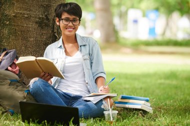 Kampüste oturan ve bir kitap okuma bardaklarda oldukça Endonezya kız öğrenci