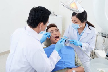 Dentist and nurse using mouth mirror, suction tube and dental explorer when examining teeth of patient clipart
