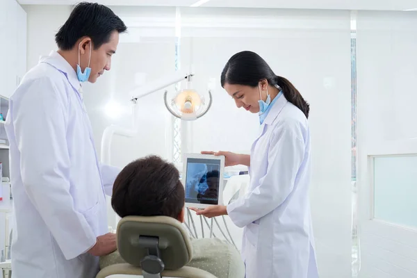 Smiling Asian dentist showing jaw x-ray to patient