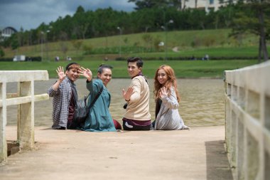 Nehir iskele üzerinde oturan ve kameraya bakarak mutlu Vietnamca genç insanlar