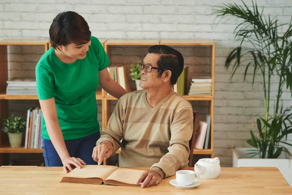 Asiático Mujer Con Senior Hombre Leyendo Libro Casa Hombre Apuntando —  Fotos de Stock