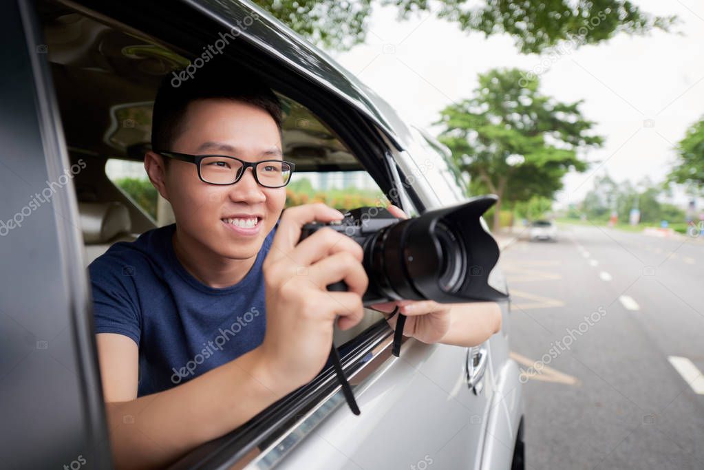 Vietnamese young man with digital camera taking photos during car trip