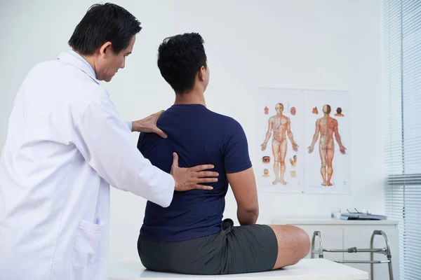 年間の診療内で若い男の背骨をチェックする医師 — ストック写真