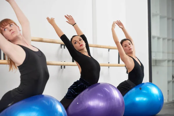 Women performing exercise on fit ball at ballet class